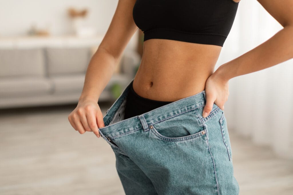 Faceless woman wearing baggy jeans after weight loss