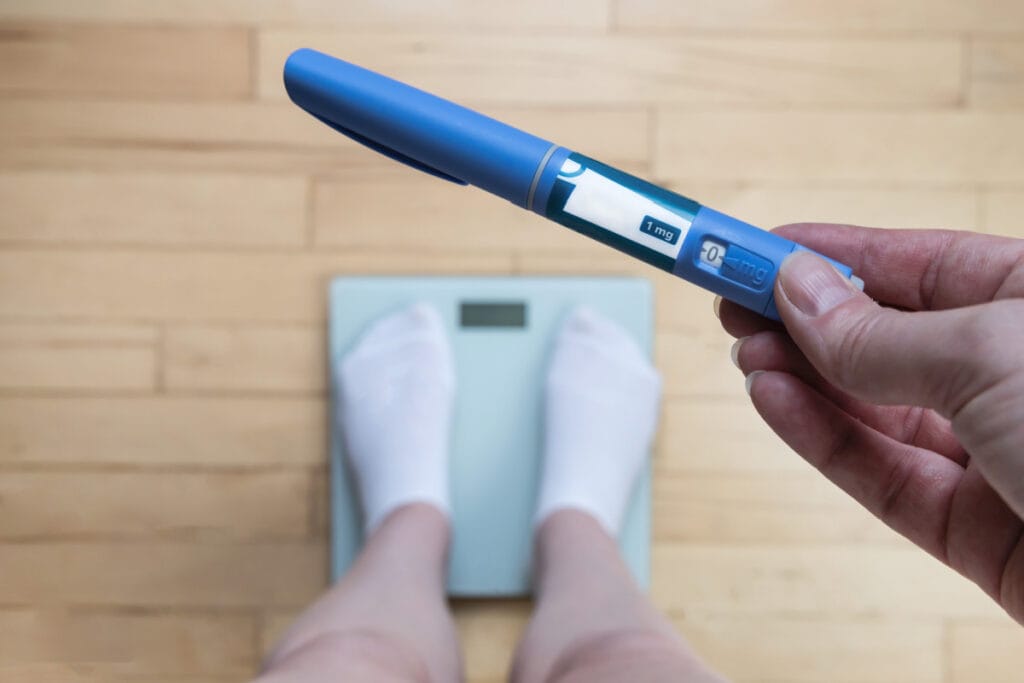 Person holding semaglutide weight loss cartridge while standing on scale